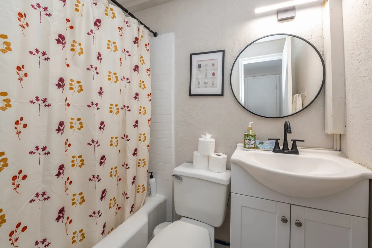 This image captures a modern bathroom interior with a decorative shower curtain, a round mirror above the sink, and a sleek faucet. The space feels airy and inviting, with a fresh and cozy mood that emphasizes cleanliness and comfort. Towels are neatly arranged, and the overall setup supports both quick morning routines and relaxing baths.