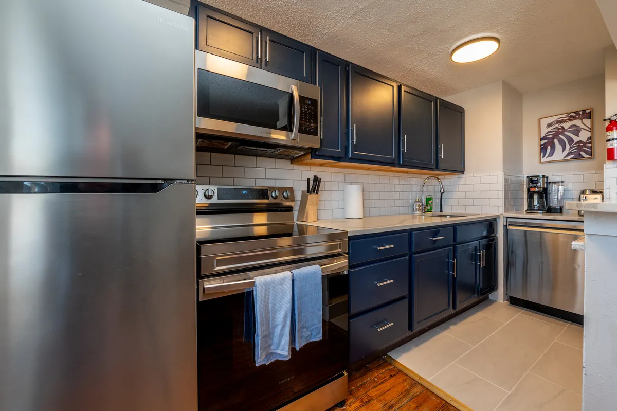 This image showcases a modern kitchen featuring stainless steel appliances, navy blue cabinetry, and a countertop set with kitchenware. The arrangement suggests a functional and inviting workspace, perfect for preparing meals or entertaining guests.