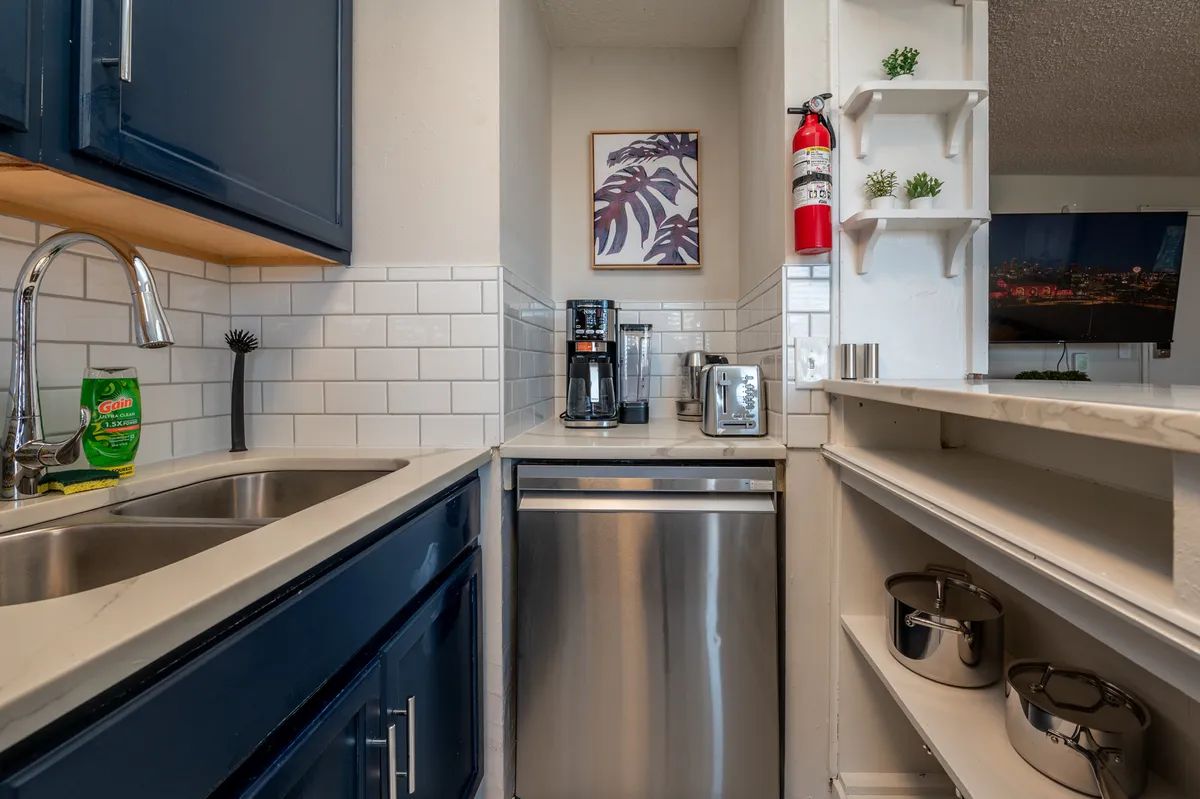 A close-up of a kitchen area with dark blue cabinetry, stainless steel appliances, and decorative wall art. The scene is practical and inviting, suggesting a space designed for daily rituals like brewing coffee or sharing casual meals.